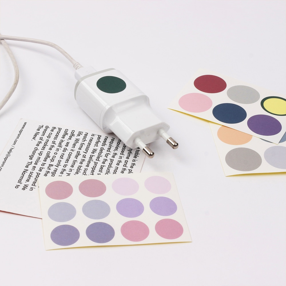 Color Mood Sticker M2 auf einem Tisch mit einem Ladenetzteil, das mit einem gruenen Punktaufkleber markiert ist. 